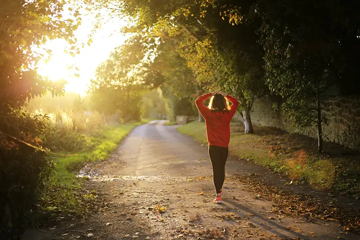 Frau in roter Sportkleidung beim Spaziergang auf sonnigem Waldweg als Symbol für Longevity und ganzheitliche Gesundheit im Alltag